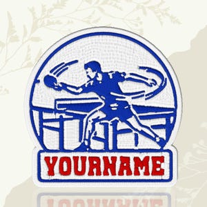 May include: Embroidered patch featuring a blue ping pong player in action, set against a white background within a blue circle. The patch includes the text "YOURNAME" in red letters on a white and blue rectangle, suitable for sports enthusiasts.