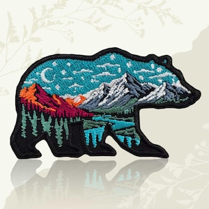 May include: Embroidered bear-shaped patch with a mountain landscape design. The black bear has an interior scene of mountains, trees, a lake, and a night sky with a crescent moon and stars. Ideal for jackets, bags, or other fabric items. Measurements are in centimeters.