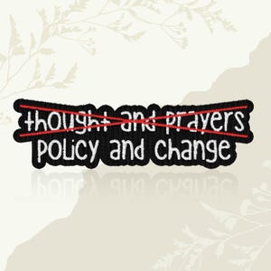 May include: A black embroidered patch with the words "thought and prayers" crossed out in red, replaced by "policy and change" in white. The patch has a black border and is set against a neutral background.
