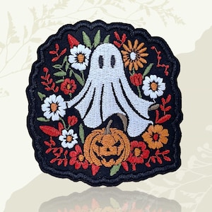May include: Embroidered patch with a white ghost, a smiling pumpkin, and colourful flowers on a black background. The patch has a scalloped edge, ideal for Halloween or the spooky season.