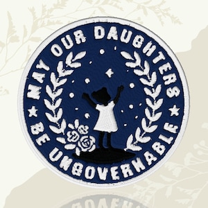 May include: Circular embroidered patch with a navy blue background and white text: "MAY OUR DAUGHTERS BE UNGOVERNABLE." A silhouette of a girl in a white dress with arms raised is in the centre. The patch has a white border and floral accents.
