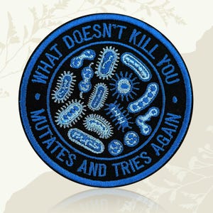 May include: A circular embroidered patch with a black background and a bright blue border. The text "WHAT DOESN'T KILL YOU MUTATES AND TRIES AGAIN" is stitched in blue around the edge, surrounding various blue illustrations of bacteria.