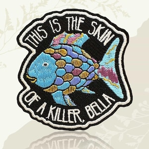 May include: Embroidered patch with a vibrant fish design in shades of blue, purple, and gold. The patch is edged in black and white, with the text "THIS IS THE SKIN OF A KILLER, BELLA" in a circular arrangement.