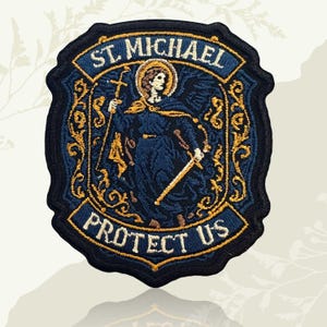 May include: Embroidered patch featuring St. Michael, holding a cross and sword, with the text "ST. MICHAEL PROTECT US." The patch is navy blue with gold and white accents, and a black border. The design is detailed and ornate.