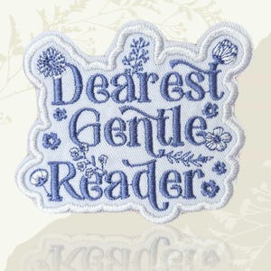 May include: Embroidered patch with the words "Dearest Gentle Reader" in blue script. The patch has a white border with floral accents and is shaped like a cloud. The background is a light beige.