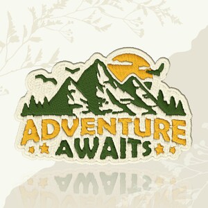 May include: Embroidered patch with a mountain scene, a yellow sun, and the text "ADVENTURE AWAITS". The patch is in green and yellow with a cream border. Includes two small stars.