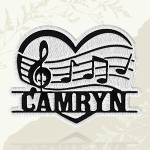 May include: Black and white embroidered patch in the shape of a heart, featuring musical notes and the name "CAMRYN". The design includes a treble clef and musical notes on a staff.