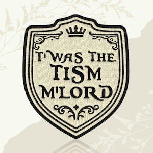May include: Embroidered patch in the shape of a shield, featuring the text "I WAS THE TISM M'LORD" in black thread. The shield has a cream-colored background with black decorative borders and a crown at the top.