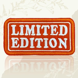 May include: An orange rectangular patch with the words "LIMITED EDITION" embroidered in white. The patch has a white border and a thin orange outline. The patch is likely for clothing or accessories.