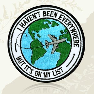 May include: Embroidered patch with a white border and the text "I HAVEN'T BEEN EVERYWHERE BUT IT'S ON MY LIST". The patch features a green and blue world map with a grey aeroplane.