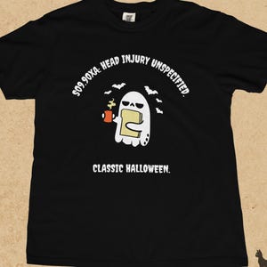 Puede incluir: Una camiseta negra de manga corta con un gráfico de un fantasma blanco que sostiene una tostada y una taza roja. El texto dice S09.90XA: HEAD INJURY UNSPECIFIED. CLASSIC HALLOWEEN. Pequeños murciélagos negros rodean al fantasma en la prenda.