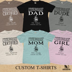 May include: Six short-sleeved t-shirts in various colors including black, gray, light blue, and beige. Each shirt features a graphic of a microscope, the text CYTOTECHNOLOGIST followed by a title like DAD or CERTIFIED, and a name with SCREENING SINCE 2020.
