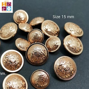 Puede incluir: Una colección de botones metálicos dorados, cada uno con un diseño en relieve. Los botones miden aproximadamente 1,5 cm de diámetro y presentan un escudo detallado. La imagen incluye el texto "Size 15 mm".
