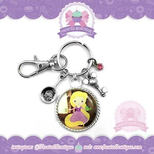 Peut inclure: Un porte-clés argenté avec un charme rond représentant une image de dessin animé de Raiponce du film Disney Tangled. Le charme a une bordure argentée et un strass rose. Le porte-clés comprend également un charme cuillère en argent, un charme clé en argent et un fermoir en argent.