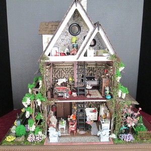 May include: A miniature dollhouse with a white exterior and a green ivy-covered facade. The dollhouse is open to reveal a multi-level interior with furnished rooms, including a living room, bedroom, and kitchen. The dollhouse is set on a base with a miniature garden.
