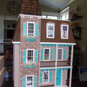 May include: A dollhouse with a brown shingled roof, white trim, and turquoise shutters. The dollhouse has three floors and a balcony on the second floor. The dollhouse is made of wood and has a brick facade.