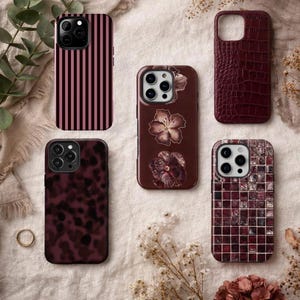 May include: Five smartphone cases in various dark red and burgundy patterns: one with black vertical stripes, one with a dark floral print, one with a crocodile skin texture, one with a dark tortoiseshell pattern, and one with a dark mosaic tile design.