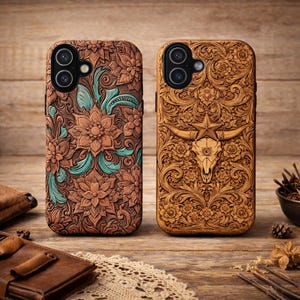 May include: Two brown leather phone cases with intricate floral and skull designs. One case features a floral pattern with teal accents, while the other showcases a steer skull with a star. Both cases are on a wooden surface.