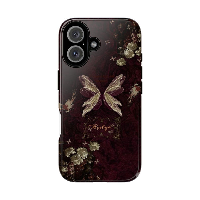 May include: A phone case with a dark burgundy background featuring a butterfly design with white and gold accents. The case has a floral pattern and the word "A&ccedil;elya" is written in cursive.