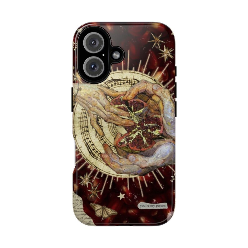 May include: A phone case featuring a detailed artistic design. The case showcases a central image of hands holding a pomegranate, set against a backdrop of a vintage-style illustration with musical notes and star accents. The text "you're my person" is visible.