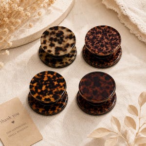 May include: Four round phone grips with a tortoiseshell pattern in shades of brown and tan. The grips are on a light beige surface, with a small card that reads "thank you" and "for supporting small business."