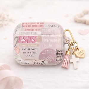 May include: A clear case for wireless earbuds, featuring a pink and white design with religious text and floral accents. Includes a gold-tone keychain with a pink tassel, cross, and heart charm that reads "God is love."