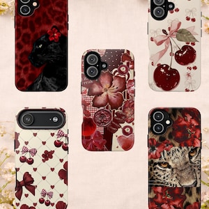 May include: A collection of phone cases with various designs. One case features a black panther with a red flower, another has cherries and bows, and others showcase floral and animal print patterns in shades of red and brown.