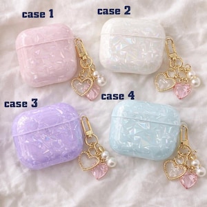 May include: Four iridescent AirPod cases in pink, white, purple, and blue, each with a gold-coloured keychain. The keychains have heart-shaped charms and faux pearls. The cases are labelled "case 1", "case 2", "case 3", and "case 4".