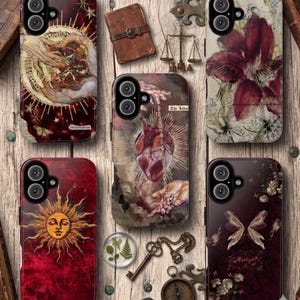 May include: A collection of phone cases with unique designs. The cases feature illustrations of a sun, butterflies, and anatomical hearts. Other cases display hands, flowers, and celestial elements. The color palette includes burgundy, gold, and cream.