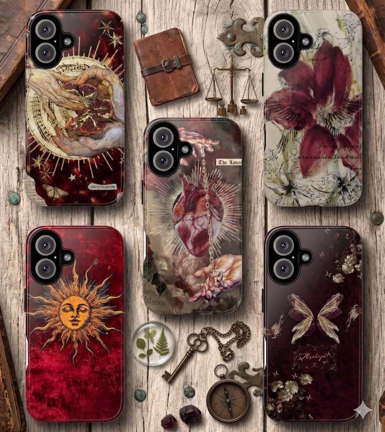 May include: A collection of phone cases with unique designs. The cases feature illustrations of a sun, butterflies, and anatomical hearts. Other cases display hands, flowers, and celestial elements. The color palette includes burgundy, gold, and cream.
