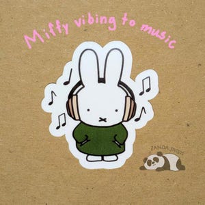May include: A white bunny sticker with headphones, wearing a green dress, and musical notes. The text "Miffy vibing to music" is written above the bunny. A panda sticker is in the bottom right corner. The sticker is on a brown background.