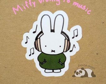 May include: A white bunny sticker with headphones, wearing a green dress, and musical notes. The text "Miffy vibing to music" is written above the bunny. A panda sticker is in the bottom right corner. The sticker is on a brown background.