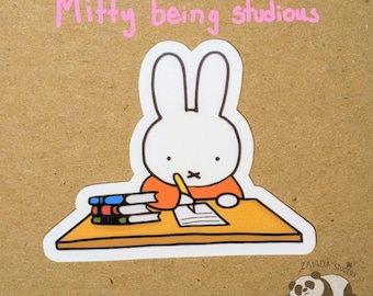 May include: A sticker featuring a cartoon rabbit, writing at a desk with a stack of books. The text "Miffy being studious" is above the rabbit. A small panda sticker is in the bottom right corner.