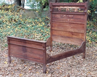 Puede incluir: Un marco de cama de madera vintage con una cabecera y un piecero tallados. El marco es marrón y tiene un acabado desgastado. La cama está sentada sobre un lecho de hojas caídas.