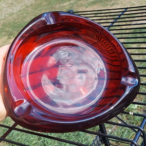 May include: A triangular red glass ashtray with a smooth, shiny surface. The ashtray is approximately 6 inches in diameter.