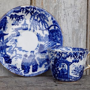 Könnte beinhalten: Ein blaues und weißes Porzellan-Teetassen- und Untertassen-Set mit japanisch inspiriertem Design. Das Set zeigt ein zartes Blumenmuster und eine Szene mit einer Pagode und einer Brücke.