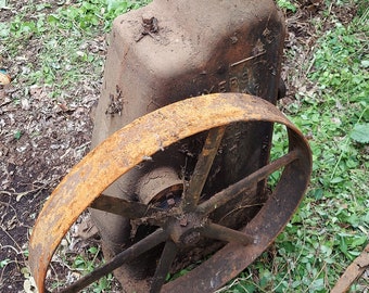 May include: A rusty, antique engine with a large, round wheel. The engine is made of cast iron and has a metal handle. The wheel is made of metal and has a wooden rim. The engine is sitting on a bed of green grass.