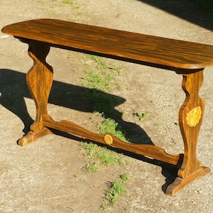 May include: A long, wooden console table with a dark brown stain. The table has a curved top and decorative carvings on the legs.