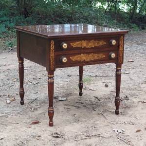 May include: A dark brown wooden end table with two drawers. The drawers have gold painted floral designs and gold knobs. The table has turned legs with gold accents.