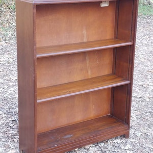 May include: A wooden bookcase with three shelves. The bookcase is dark brown and has a simple design.