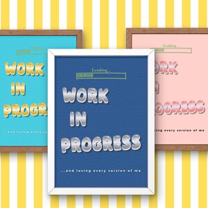 May include: Three framed art prints with the words "WORK IN PROGRESS" in bold, stylized lettering. The prints feature backgrounds of blue, pink, and teal, with a yellow and white striped background. The phrase "...and loving every version of me" is at the bottom.