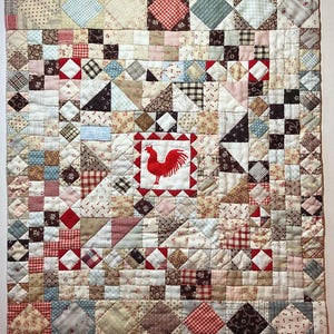 May include: A patchwork quilt with a rooster design. The quilt features a variety of fabrics in red, white, blue, and brown. The center square showcases a red rooster. The quilt is made of small squares and triangles.