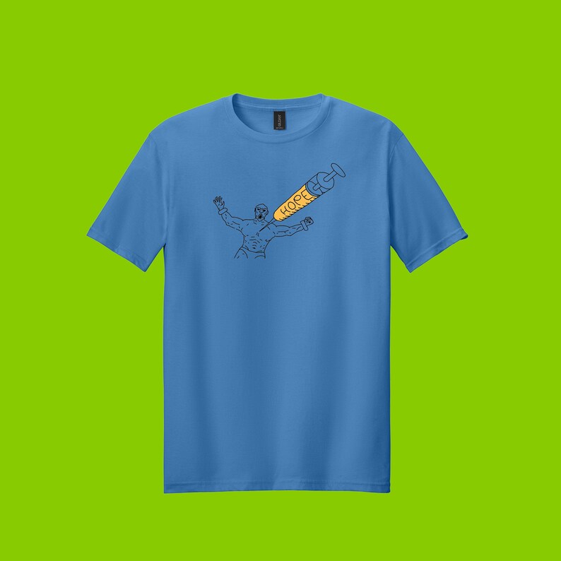 May include: Sky blue t-shirt featuring a black line drawing of a person with arms raised, and a syringe with the word "HOPE" in orange. The syringe is pointing towards the person. The shirt is on a green background.