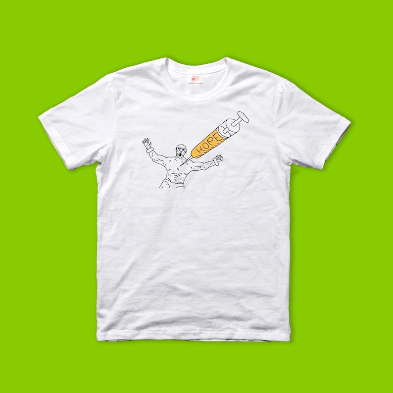 May include: White t-shirt featuring a black and yellow illustration. The graphic depicts a muscular figure with arms raised, pierced by a syringe labeled "HOPE". The syringe is yellow with black outlines. The shirt has a crew neck.