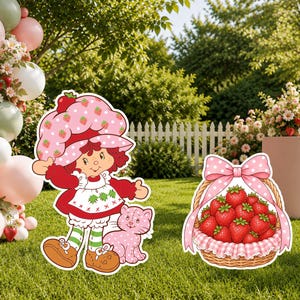 May include: A decorative cutout of a character with red hair wearing a strawberry-patterned hat, a red dress, and green striped leggings, standing next to a pink cat and a woven basket filled with red strawberries and a pink polka-dot bow.