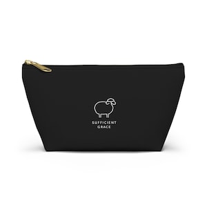 May include: Black zippered pouch with a gold-colored zipper. The pouch features a white line drawing of a sheep and the words "SUFFICIENT GRACE" in white, centered below the sheep illustration.