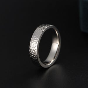 May include: A silver ring with a hammered texture. The ring has a band with a series of small, evenly spaced indentations, giving it a textured appearance. The ring is set against a dark background.