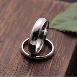 May include: Two polished silver rings, one resting atop the other, against a dark wood grain background. The rings have a smooth, reflective surface, and the top ring is slightly out of focus. The image suggests a theme of commitment or jewelry.