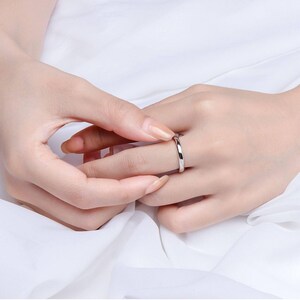 May include: A simple, polished silver ring is worn on a finger. The ring has a smooth, rounded band. The background is a soft, white fabric, creating a clean and elegant presentation. The ring is a classic piece of jewelry.
