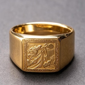 May include: A gold-toned signet ring featuring a square face with an engraved relief of a figure with long flowing hair standing near a pillar under a circular moon, surrounded by a decorative border pattern on the band's flat top surface.